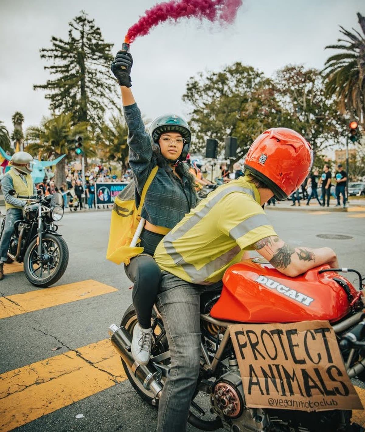 Vegan Moto Club riders on a Ducati motorcycle with a Protect Animals sign at an animal rights rally
